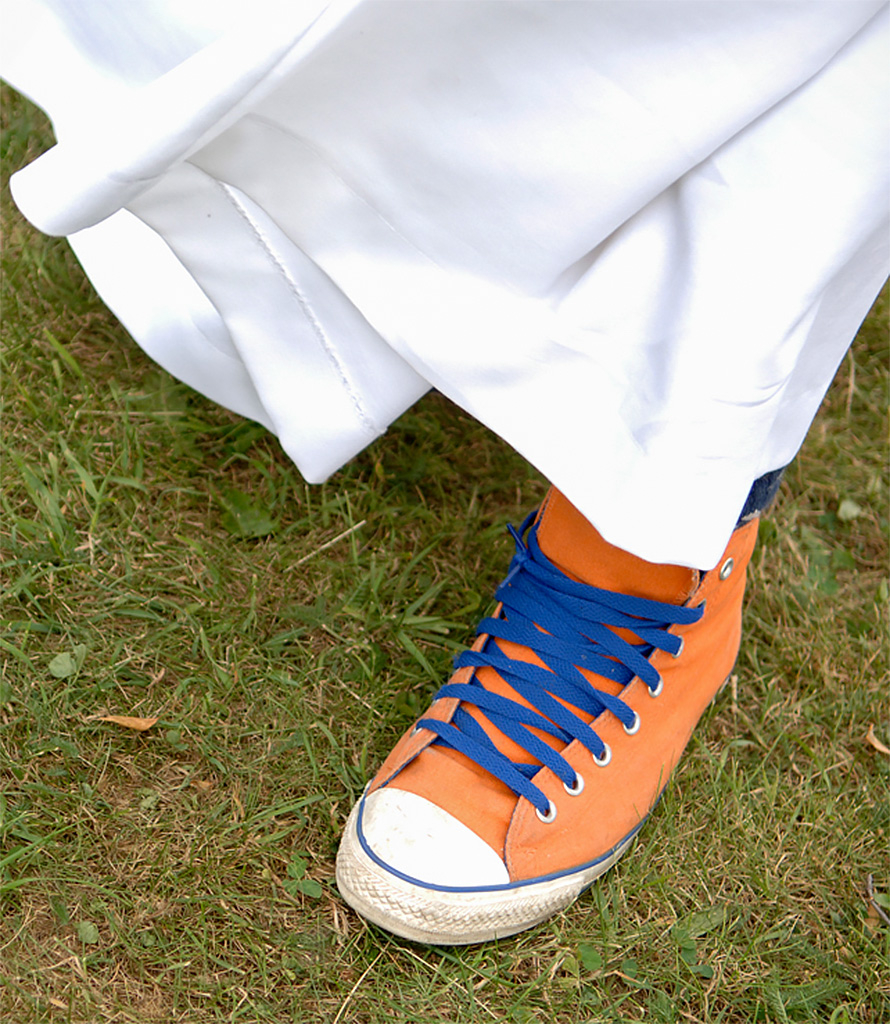 Närbild på foten av någon iklädd vit kåpa och brandgula skor med blåa snören.