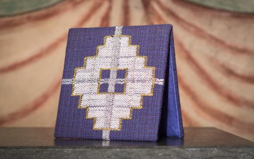 En blå textil med ett broderat kors står på ett stenaltare.