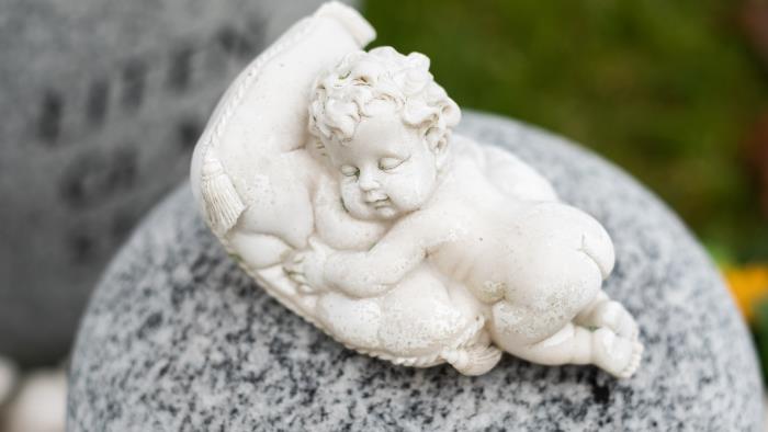 Närbild på en gravdekoration: ett liten bebis kramar en kudde.