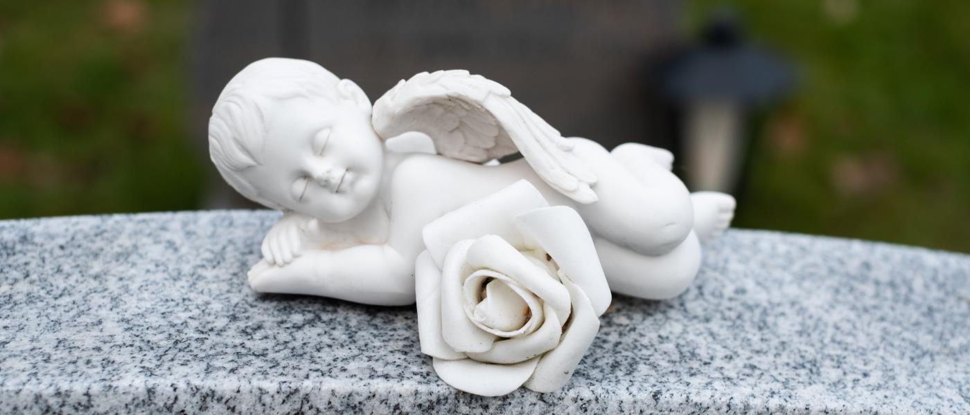 En liten sovande ängel i porslin ligger på en gravsten.