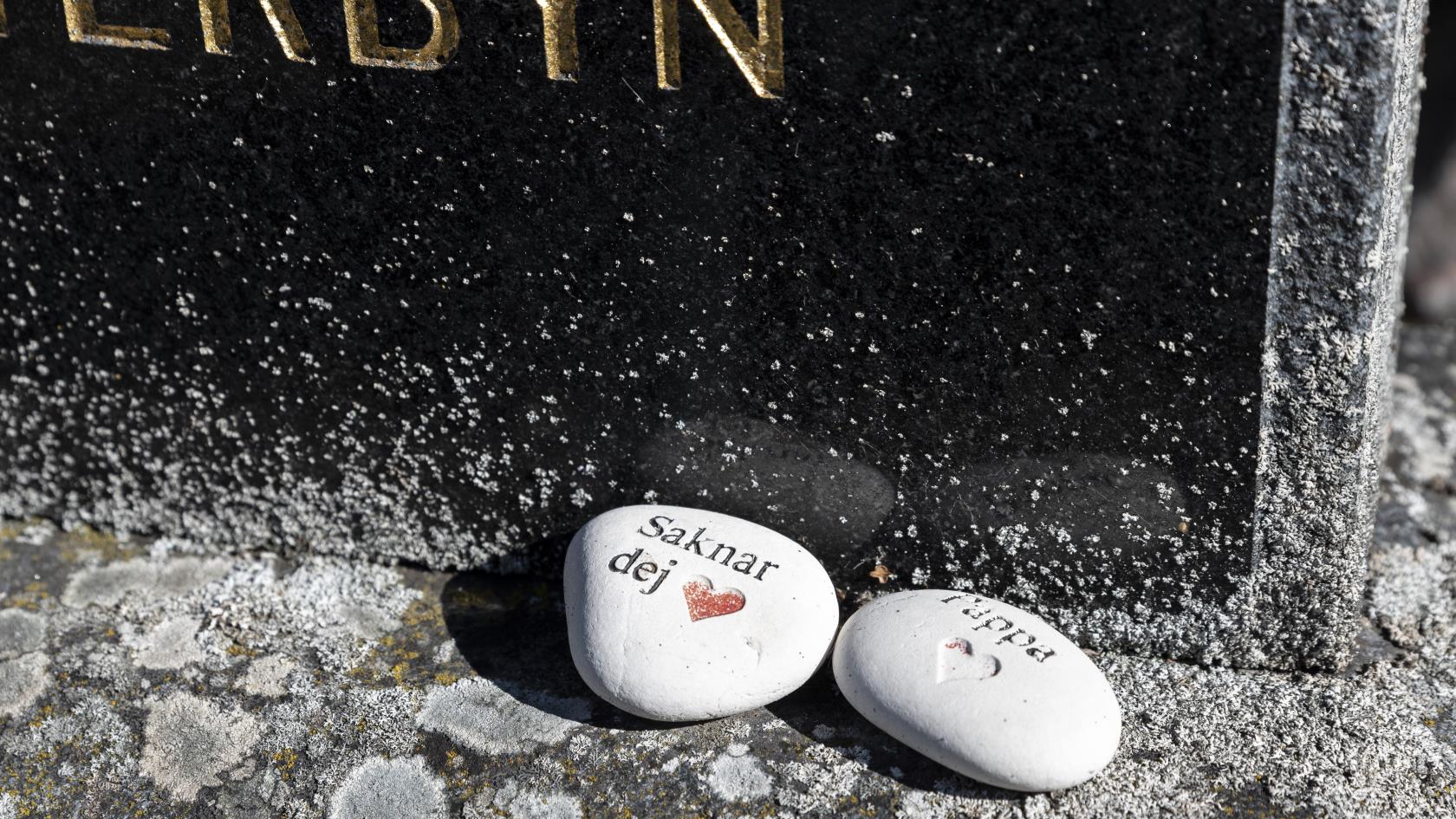 Två vita stenar med texterna Saknar dej och Pappa ligger på en gravsten.