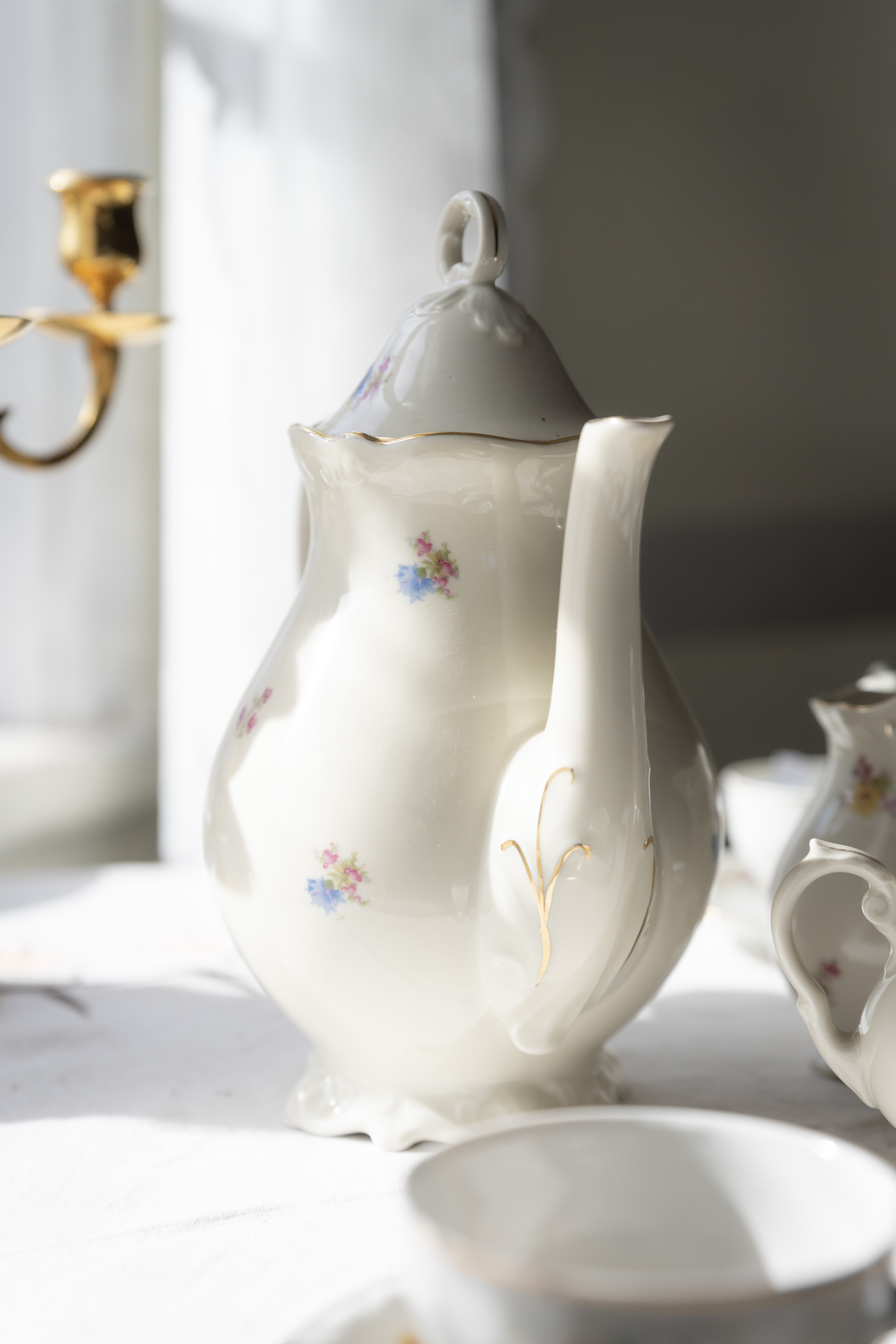 En tekanna i porslin med små målade blommor och guldiga detaljer.
