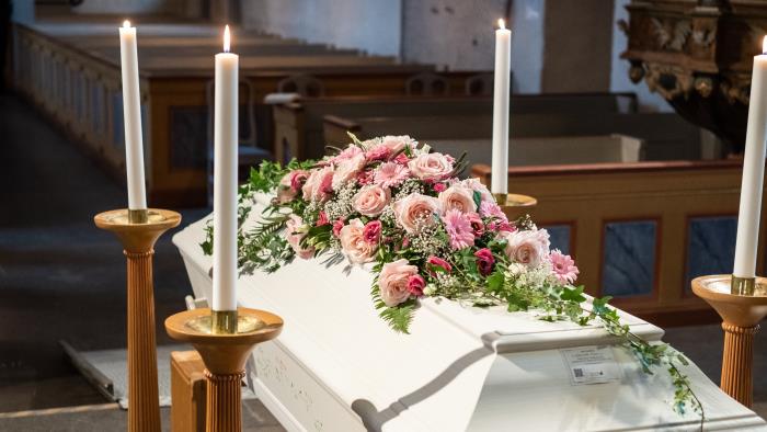 En vit kista med rosa blommor står omringad av ljus uppe vid koret.