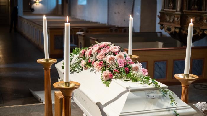 En vit kista med rosa blommor står omringad av ljus uppe vid koret.