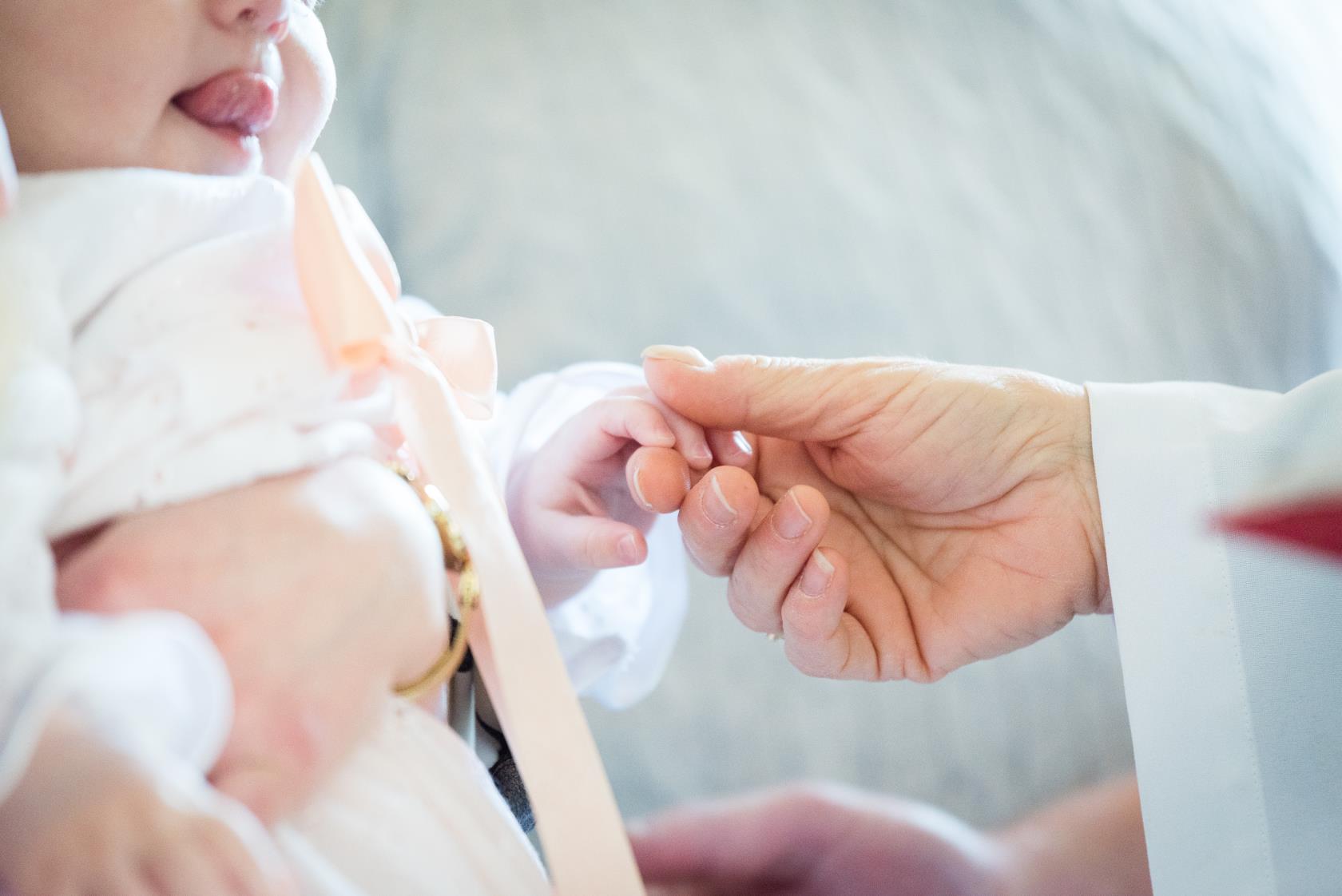 En vitklädd person håller i handen på en bebis i dopklänning.