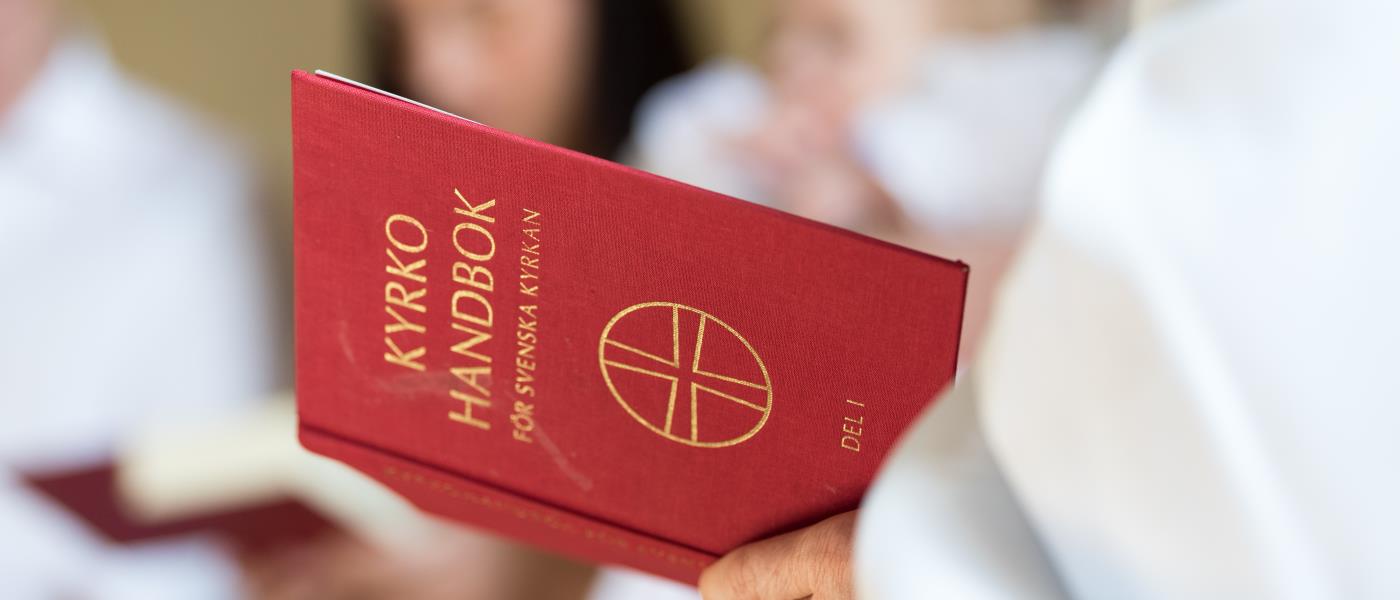 En vitklädd person håller i en kyrkohandbok.