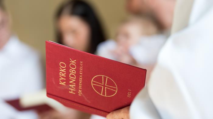 En vitklädd person håller i en kyrkohandbok.