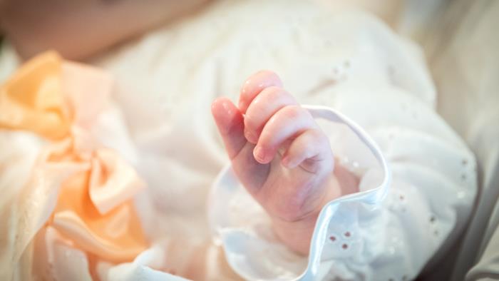 Närbild på en hand som tillhör en bebis i dopklänning.