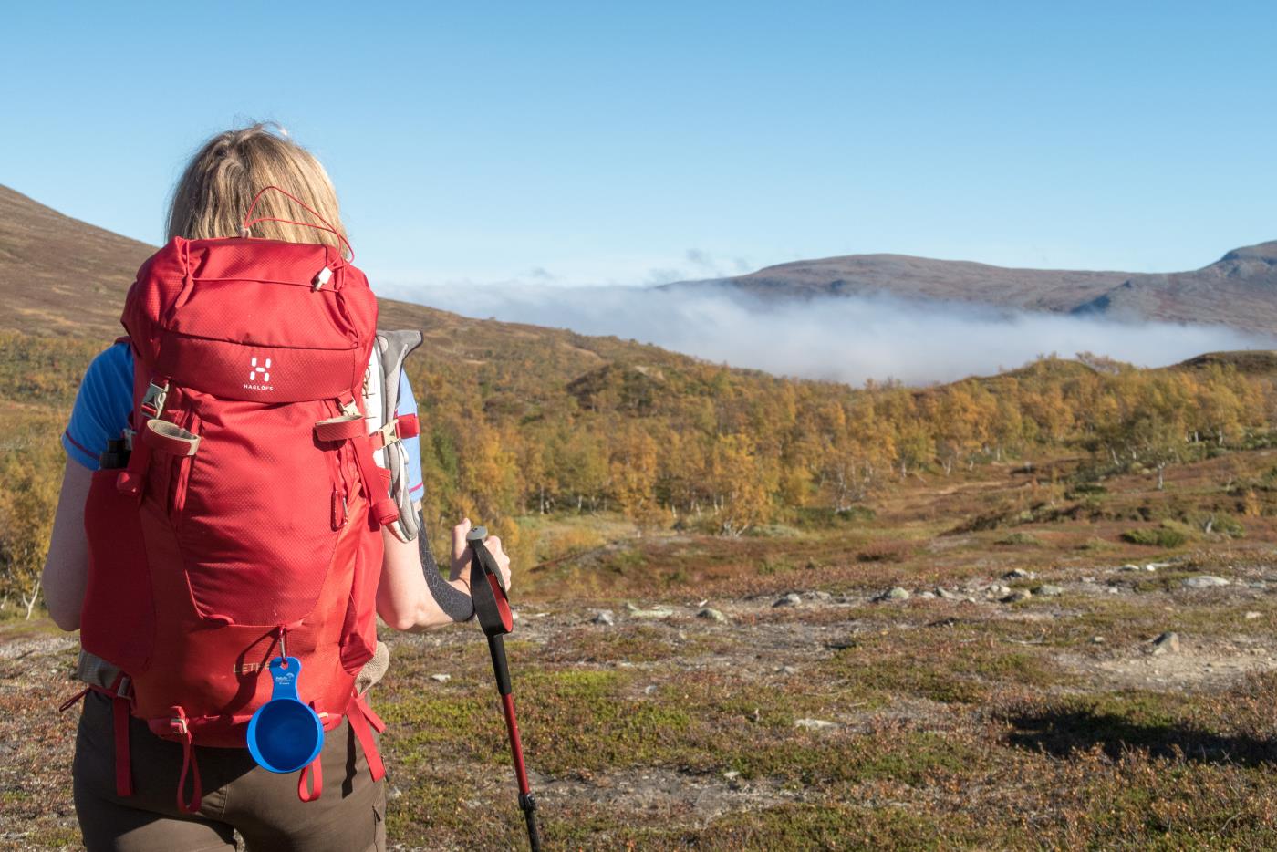 En kvinna med en stor röd ryggsäck sommarvandrar i fjällen.