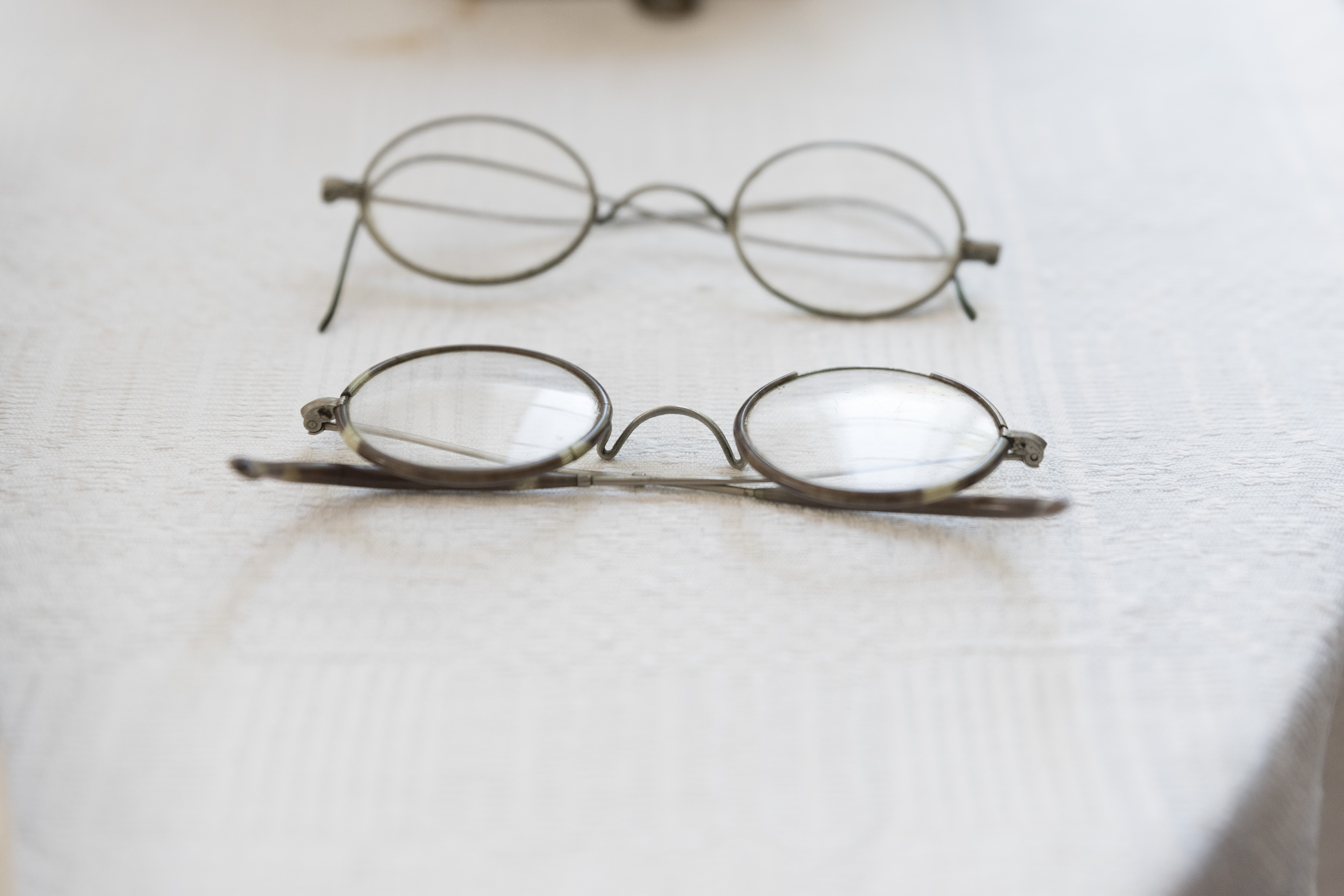 Två par runda, stålbågade glasögon ligger bredvid varandra på ett bord.