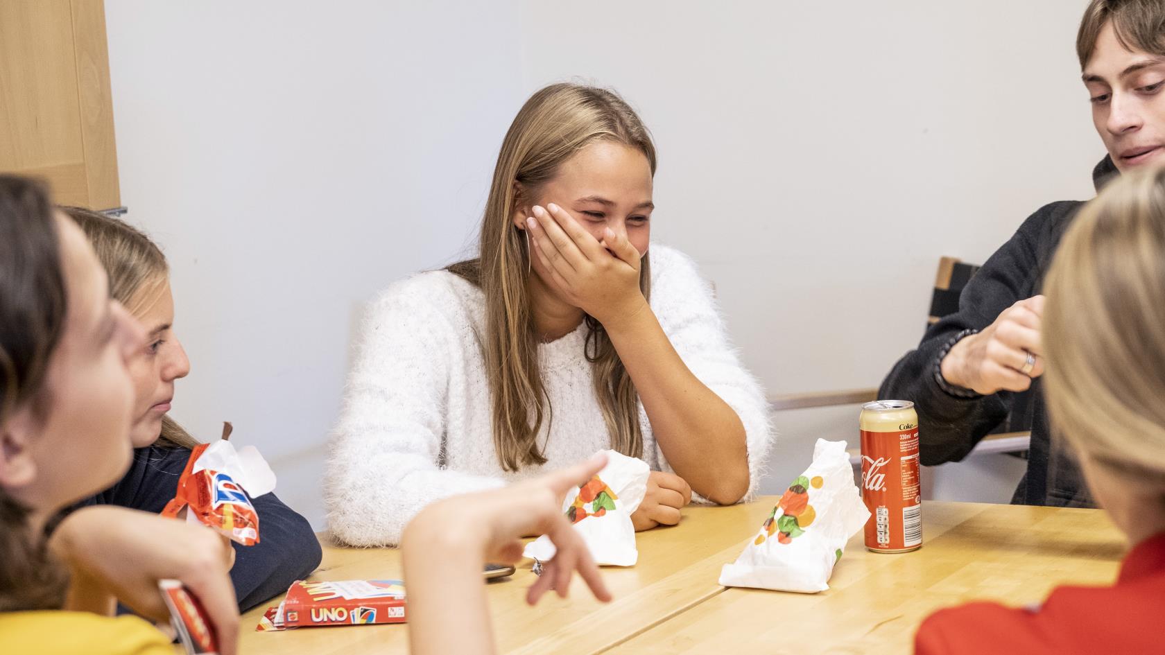Några ungdomar sitter runt ett bord och spelar Uno och äter godis.
