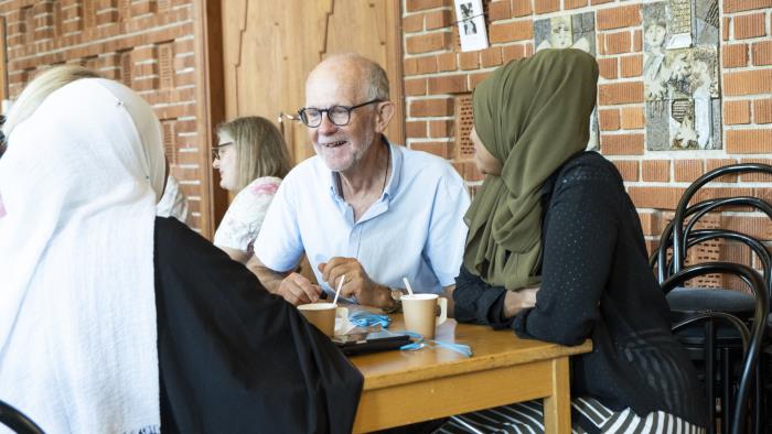 Några människor sitter vid ett bord och pratar över en kopp kaffe.