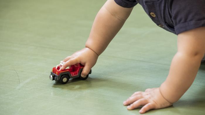 En bebis kryper på golvet med en leksaksbil.