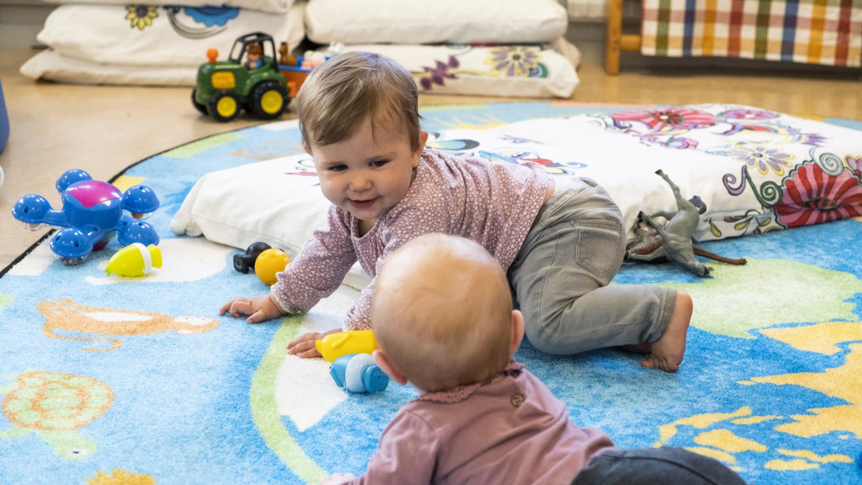 Två bebisar ligger på golvet och skrattar.