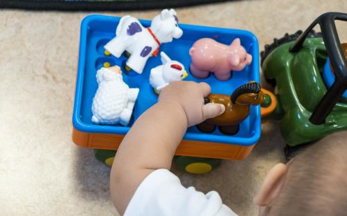 En bebis leker med en leksakstraktor med olika djur i en släpvagn.