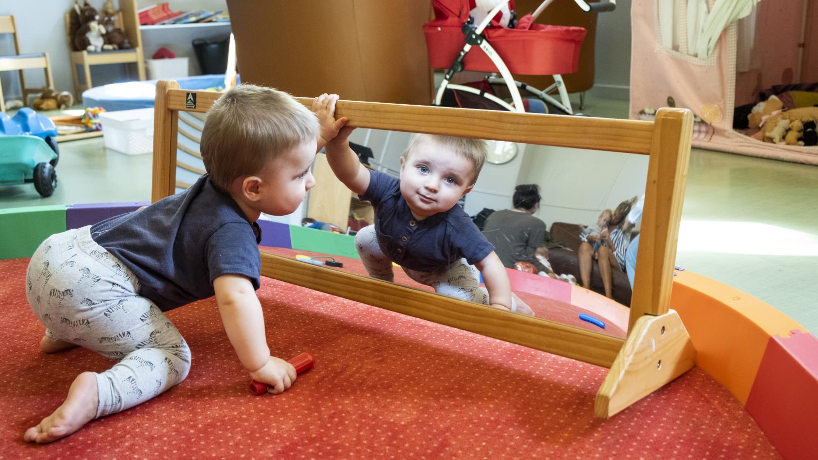 En liten pojke kryper mot en spegel på golvet.