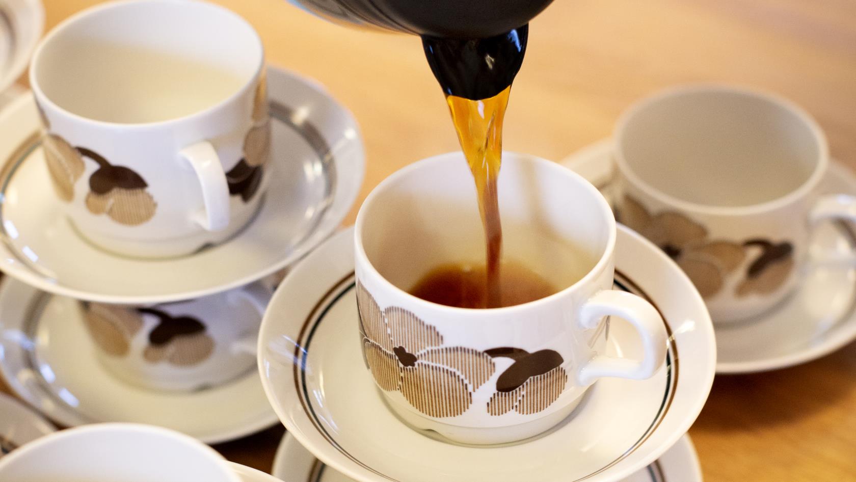 Någon häller upp kaffe i en av flera kaffekoppar som dukats fram på ett bord.