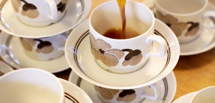 Någon häller upp kaffe i en av flera kaffekoppar som dukats fram på ett bord.