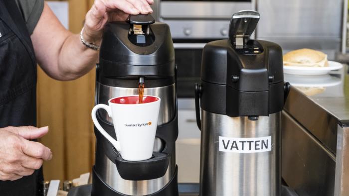 Någon pumpar kaffe ur en termos i en mugg från Svenska kyrkan.