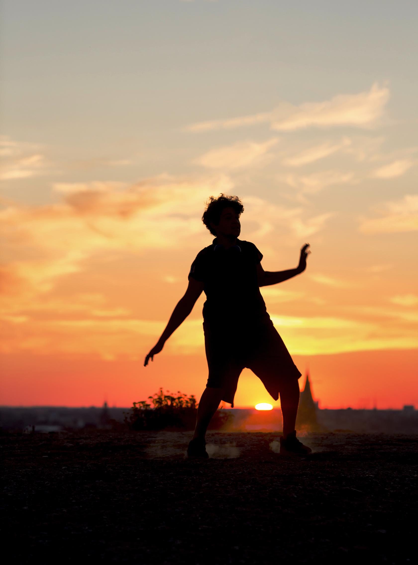 En ungdom dansar uppe på en klippa. I bakgrunden syns en stad i solnedgången.