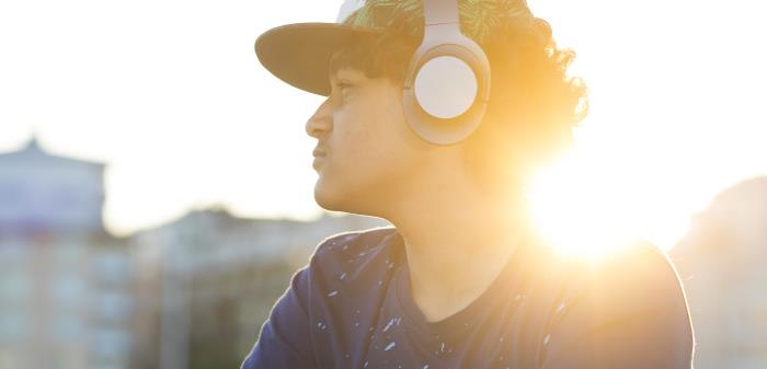 En ung kille med keps sitter i motljus och lyssnar på musik i hörlurarna.