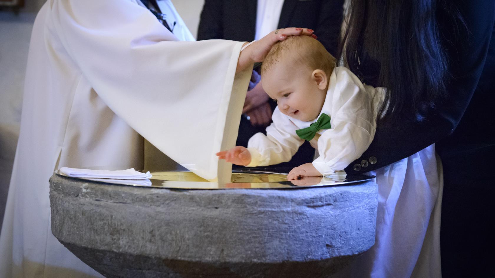 En liten bebis blir döpt. En präst håller sin hand på bebisens huvud.