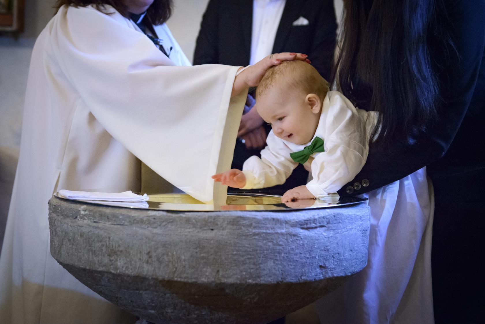 En liten bebis blir döpt. En kvinnlig präst håller sin hand på hans huvud.