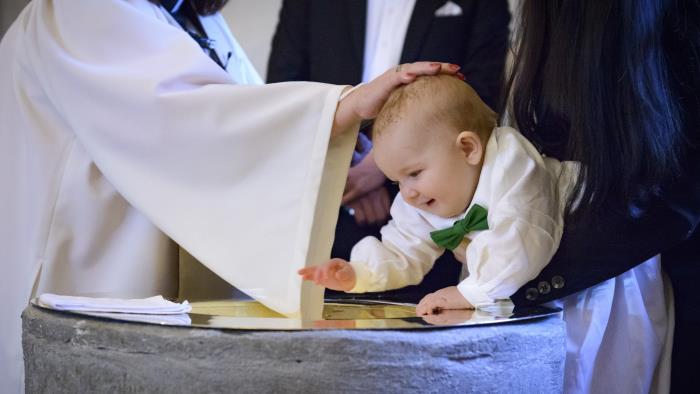 En liten bebis blir döpt. En präst håller sin hand på bebisens huvud.