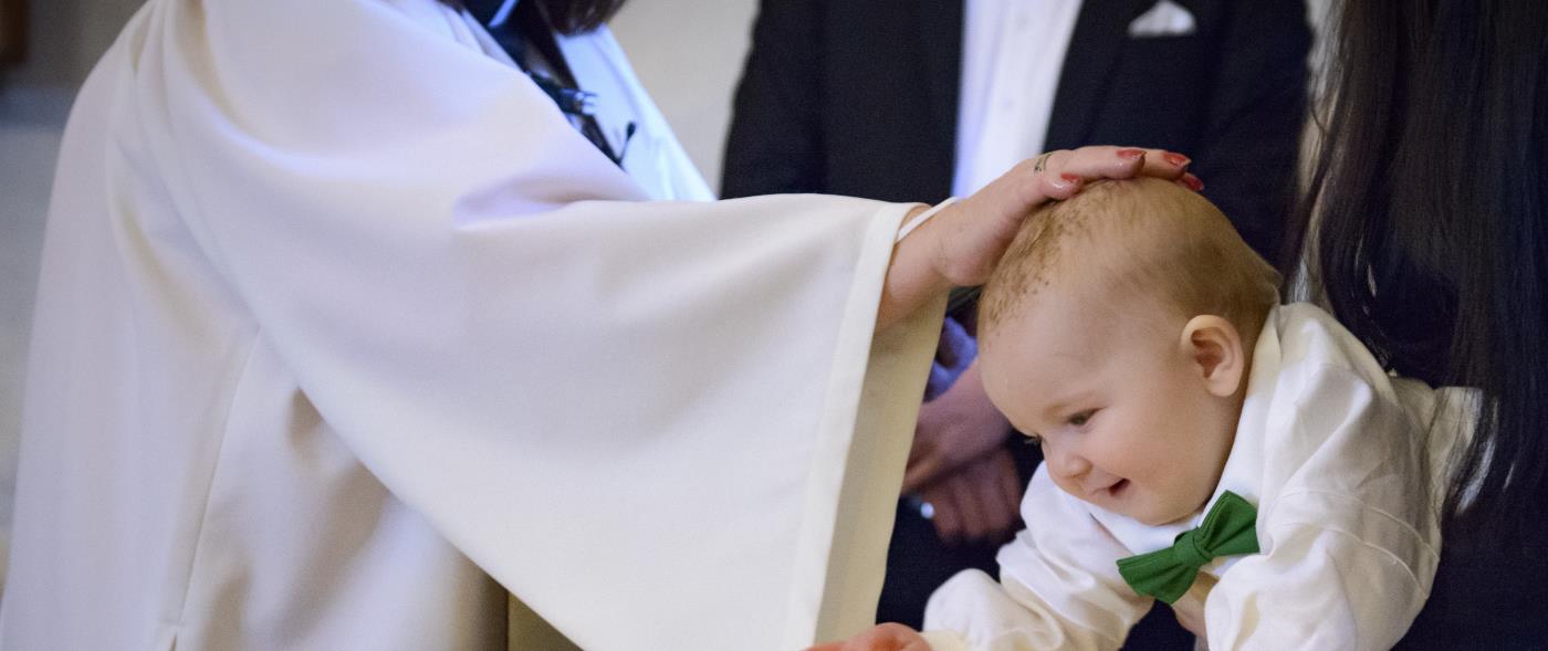 En liten bebis blir döpt. En kvinnlig präst håller sin hand på hans huvud.