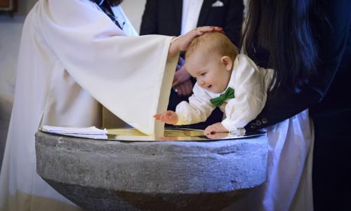 En liten bebis blir döpt. En kvinnlig präst håller sin hand på hans huvud.