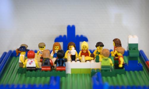 Någon har byggt med Lego: en grupp personer med olika utseenden sitter runt ett långbord.