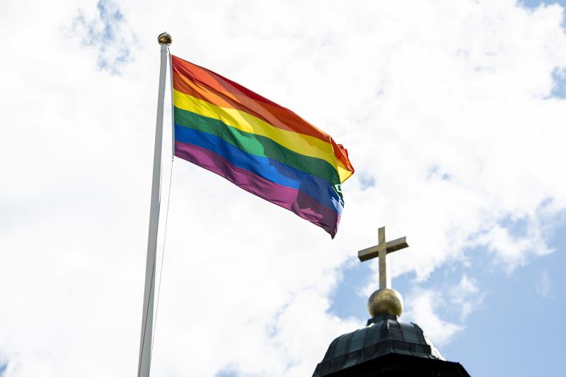 En regnbågsflagga vajar utanför en kyrka.