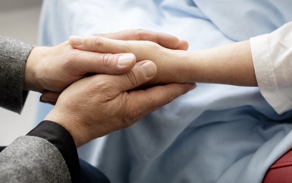 Någon håller en hand i sina vid en sjukhussäng.