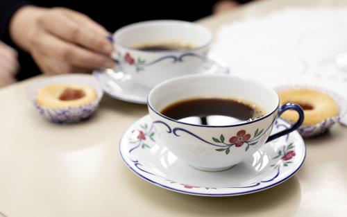 Närbild på två kaffekoppar på fat och hallongrottor.