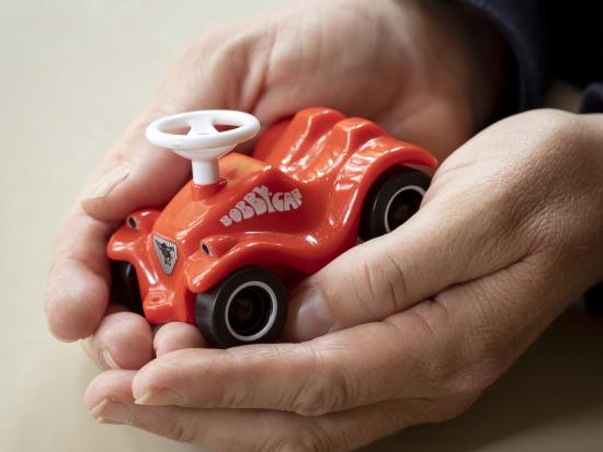 Ett par händer kupade runt en miniatyr av en röd Bobbycar.