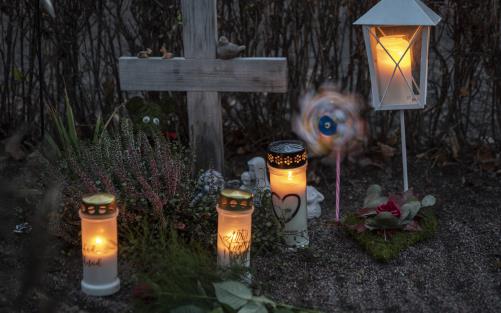 En grav med ett enkelt träkors har smyckats med gravljus, en lykta, en vindsnurra, ler- och gipsfigurer samt olika blommor.