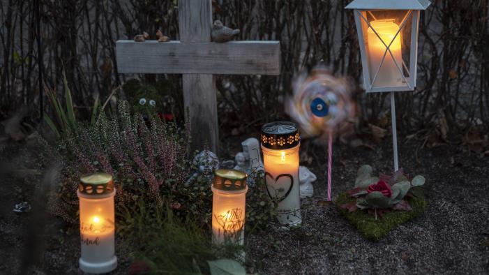 En grav med ett enkelt träkors har smyckats med gravljus, en lykta, en vindsnurra, ler- och gipsfigurer samt olika blommor.