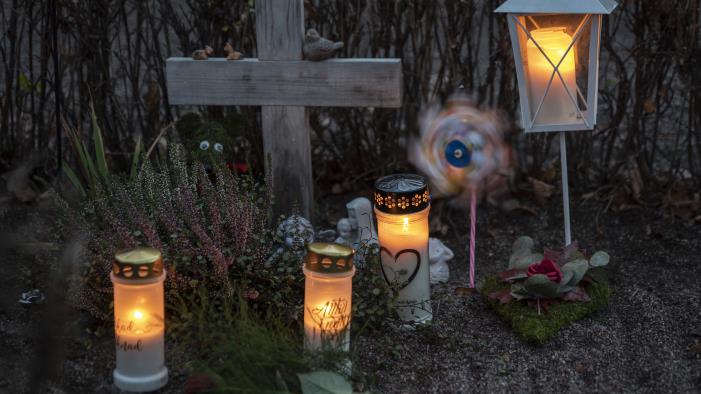 En grav med ett enkelt träkors har smyckats med gravljus, en lykta, en vindsnurra, ler- och gipsfigurer samt olika blommor.