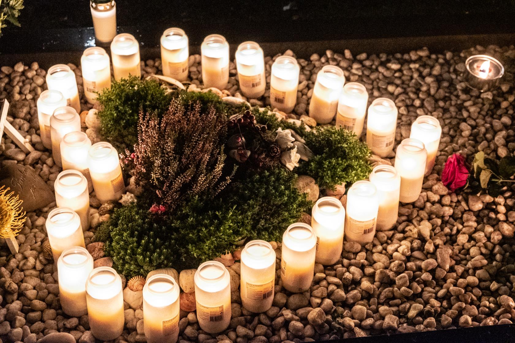 Allhelgona på kyrkogård. Människor tänder ljus på gravarna.