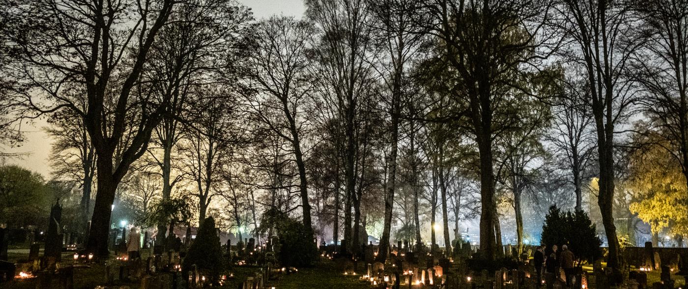Allhelgona på kyrkogård. Människor tänder ljus på gravarna.
