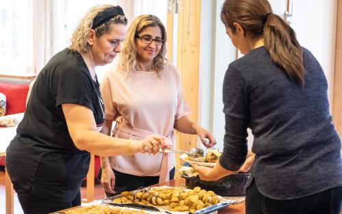 Två kvinnor serverar mat till en tredje.