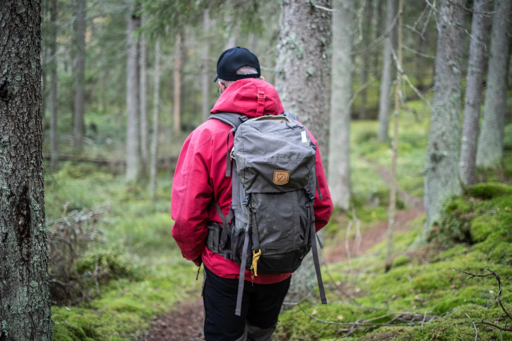 En man med ryggsäck går på en stig i skogen.