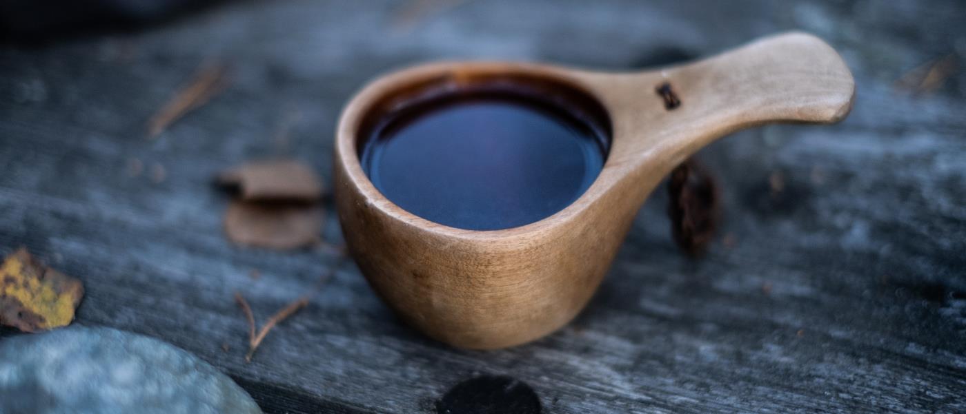 En kåsa i trä står fylld med kaffe på en träbänk.