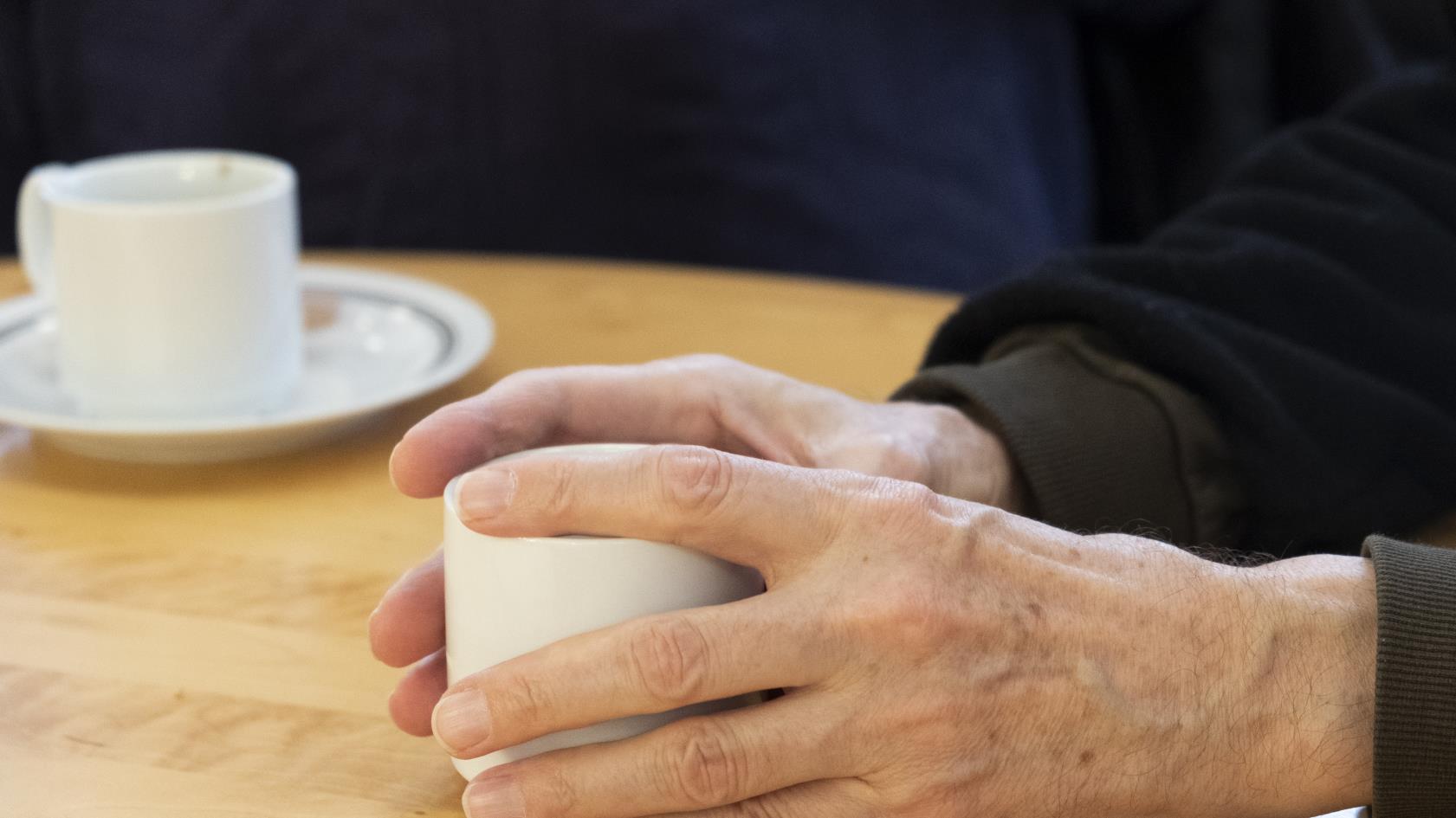 Någon håller händerna runt en kaffekopp på bordet.