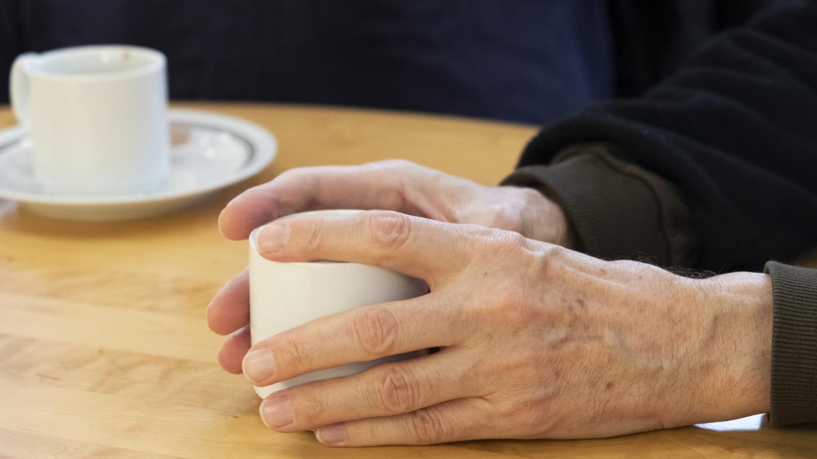 Någon håller händerna runt en kaffekopp på bordet.