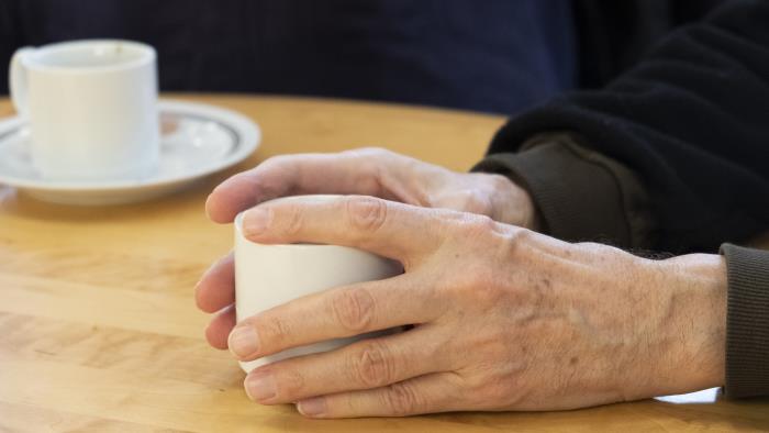 Någon håller händerna runt en kaffekopp på bordet.