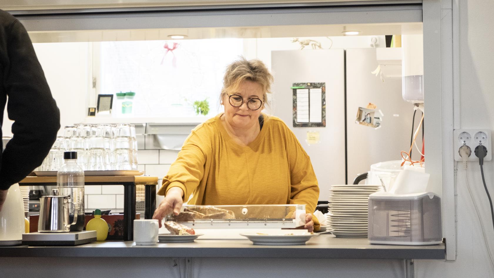 En kvinna står bakom disken och ställer fram fika.