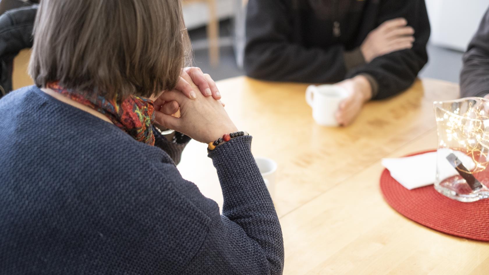 En kvinna sitter och samtalar med några andra över en kopp kaffe.
