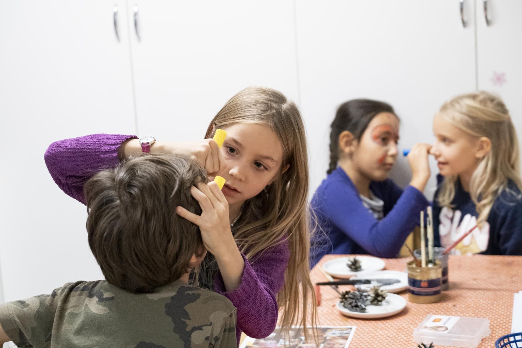 Några barn sitter och målar varandras ansikten med pennor.