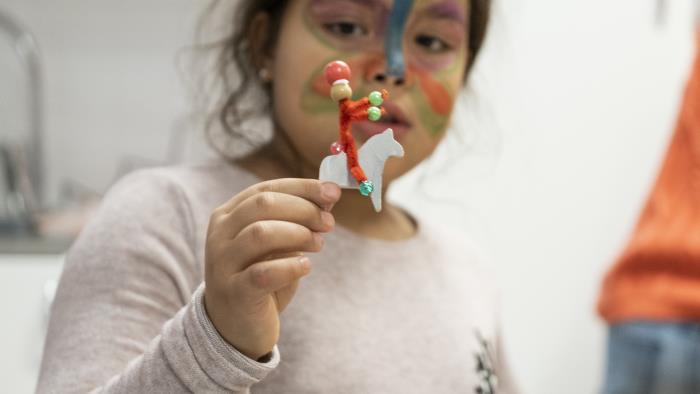 En flicka har en fjäril målad i ansiktet. Hon håller upp en gubbe gjord av piprensare.